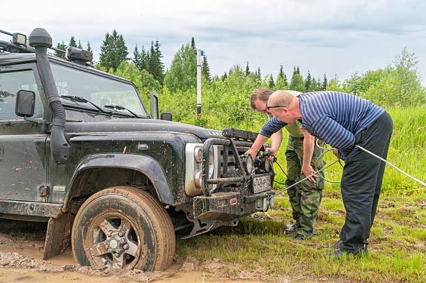 Kazovo, Russia - June 23, 2010: Two men switch on winch of all-terrain 4x4 vehicle sunk in mud against forest background.
